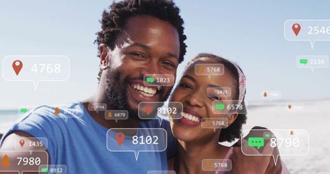 Smiling couple taking selfie on beach with social media interaction icons