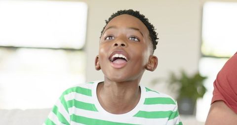 African American Boy Smiling and Looking Up on Couch, Enjoying Bright Home Moment