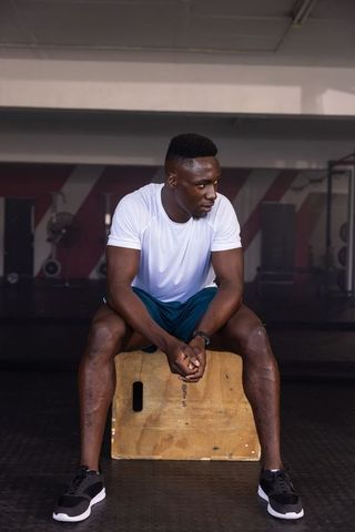Athletic male resting at gym on plyometric box for recovery