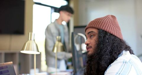 Contemplative creative professional wearing knit beanie working at laptop in modern office