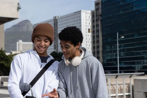 Asian and african american teen friends checking smartphone leaning on urban railing