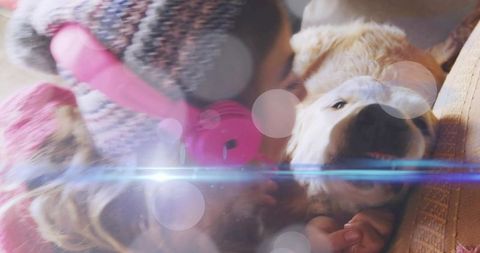 Woman wearing pink headphones cuddling light-colored dog on couch with soft bokeh warmth