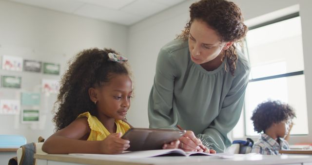 Image of happy caucasian female teacher explaining lesson to african american girl holding tablet - Download Free Stock Photos Pikwizard.com
