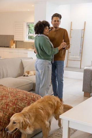 Couple slow dancing in sunlit living room with golden retriever and cozy sectional sofa