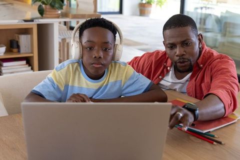 African american father tutoring son on laptop at home, online learning and homework support