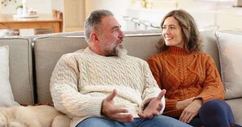 Mature couple relaxing on sofa sharing warm conversation in cozy knit sweaters at home