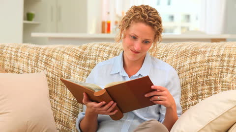 Curly-Haired Woman Engaged with Book on Cozy Sofa