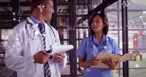Doctor and nurse reviewing medical records in glass corridor with digital data overlay