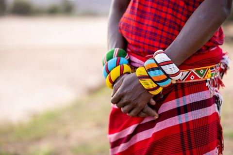 Wearing colorful beaded bangles and red checked wrap, hands clasped showcasing vibrant beadwork