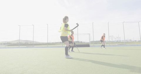 Women field hockey players practicing scrimmage on outdoor turf near goal with bright bibs
