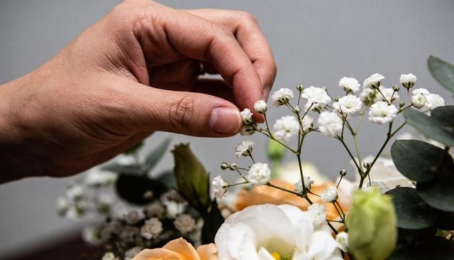 Hand arranging delicate babys breath and lisianthus bouquet with peach roses and eucalyptus