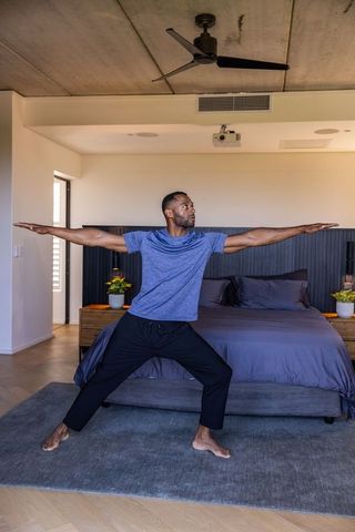 Mature african man practicing standing yoga stretch in modern minimalist bedroom