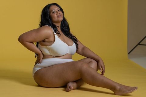 Curvy model posing confidently in white lingerie on yellow backdrop, body positive studio portrait