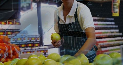 Grocery worker holding green apple and arranging fresh produce in retail produce aisle