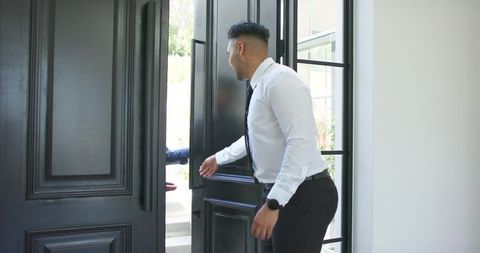 African american man in business attire opening black door welcoming visitor at home