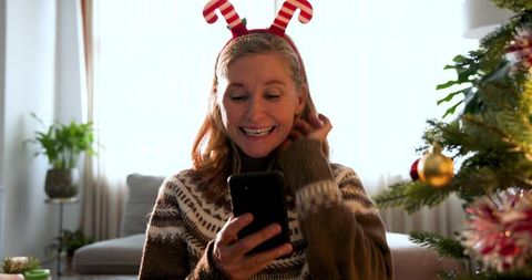 Festive Woman Smiling at Smartphone Near Christmas Tree