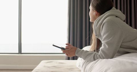 Woman Lounging on Bed with Smartphone in Serene Bright Room