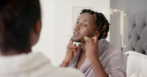 African american couple grooming together man using gua sha facial stone in bedroom
