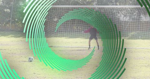 Goalkeeper Guarding Net with Soccer Ball and Green Circular Overlay on Grass Field