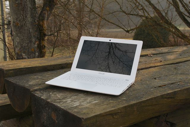 White laptop with an empty screen on a wooden table outdoors, surrounded by bare trees during winter. Ideal for depicting remote work, technology in nature, or promoting laptops and remote working solutions. Useful for advertisements or articles about digital nomads, work-life balance, and the integration of technology with natural environments.