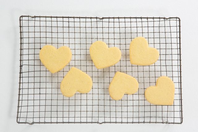 Heart shaped cookies cooling on a wire rack against a white background. Ideal for Valentine's Day promotions, baking blogs, dessert recipes, and romantic celebration themes.