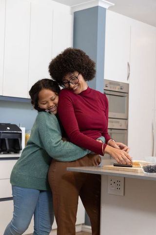 African american mother and daughter hugging in modern kitchen while preparing berry snack