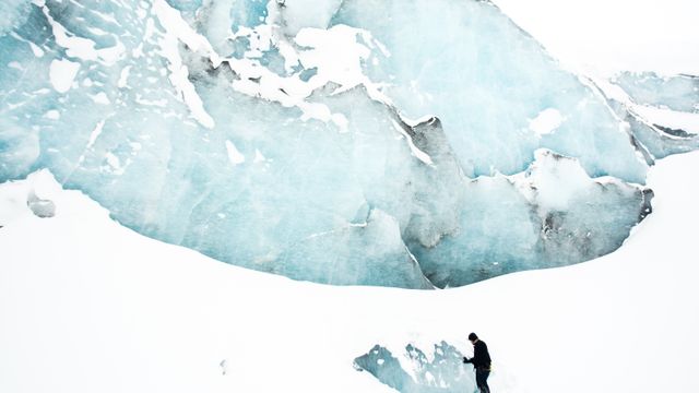 Person is exploring the icy and snowy terrain of a glacier amidst a vast and remote winter landscape. Ideal for use in content focused on adventure travel, outdoor exploration, and extreme nature conditions.