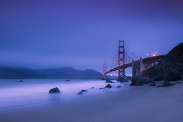 Golden Gate Bridge standing illuminated against the soft glow of twilight. Surrounded by fog, the iconic landmark appears majestic above the calm waters of the bay, blending seamlessly into the serene environment. Ideal for travel articles, tourism promotions, inspirational backgrounds, prints, and nature-themed content showcasing scenic beauty and famous landmarks.
