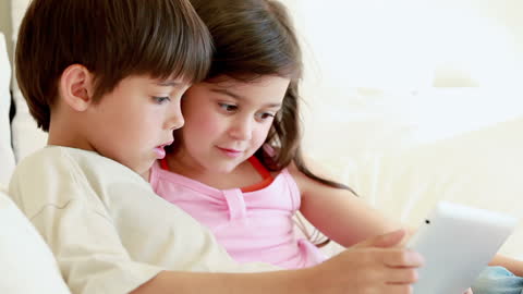 Siblings Sitting on Sofa Using Tablet Together