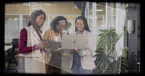 Three professional women collaborating on laptop and tablet in modern open-plan office