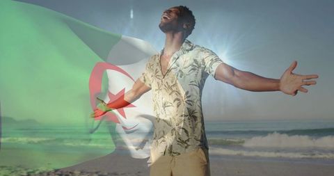 Joyful young man celebrating freedom on sunny beach with algerian flag waving and open-arms victory