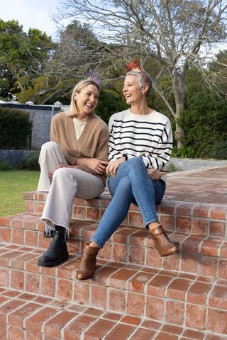 Middle-aged women laughing and chatting on red brick steps wearing party tiaras
