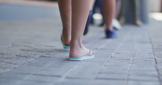 Several feet are shown walking on a paved urban sidewalk. The focus is on the footwear, with some individuals wearing flip-flops. This is useful for urban lifestyle advertisements, casual footwear promotions, or illustrating city life.