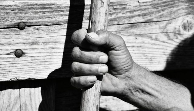 Weathered hand gripping wooden pole against barn planks casting strong monochrome shadows