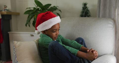 Sad boy in santa hat sitting alone during christmas time