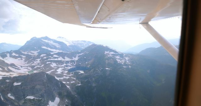 Aerial view of a mountainous landscape with patches of snow under the wing of a small aircraft, with copy space. The perspective offers a sense of adventure and exploration from the skies.