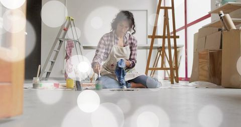 Female artist painting on floor wearing paint-stained apron and plaid shirt with easel