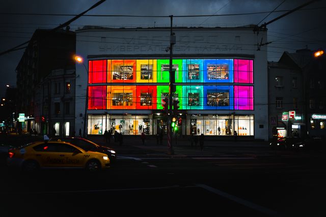 Modern building with colorful digital display lighting up facade at night in urban area. Suitable for illustrations on city nightlife, architecture, technology in design, retail spaces, and vibrant urban settings. Useful for advertising concepts, travel scenes, and technology advancements in city environments.
