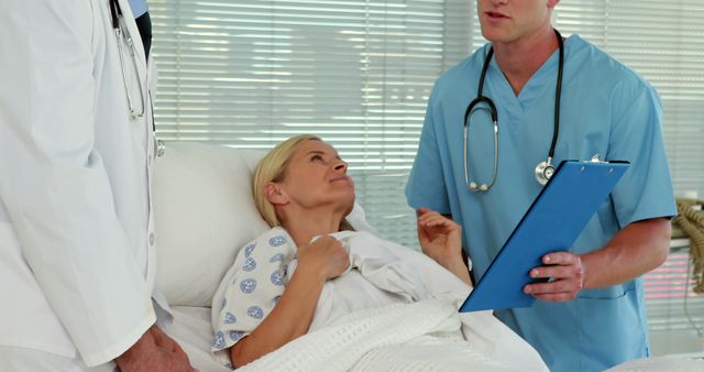 A middle-aged Caucasian woman is lying in a hospital bed while a doctor and a nurse, both Caucasian males, attend to her, with copy space. They appear to be discussing her medical condition or treatment plan.
