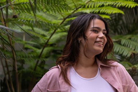Smiling young woman enjoying lush garden wearing pink shirt and white tank top
