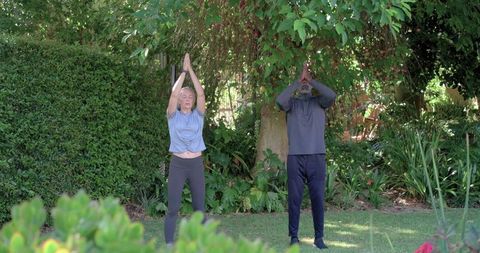 Couple practicing morning yoga stretching under lush garden canopy for wellness
