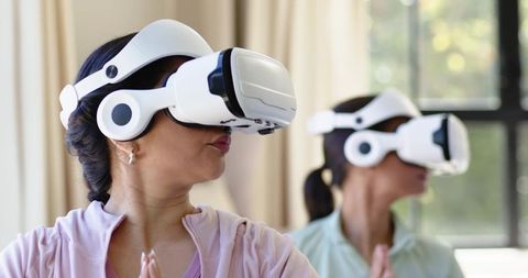 Diverse women meditating with white vr headsets in bright living room wellness scene