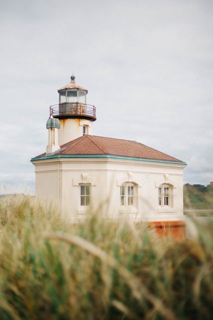 This image shows a historic lighthouse surrounded by coastal grass on an overcast day. Perfect for use in travel brochures, maritime history articles, coastal tourism promotions, and architectural studies.