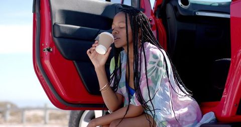 Young Woman Relaxing with Drink Next to Car in Sunlight