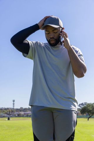 Concerned african american man talking on smartphone in sunny park wearing cap