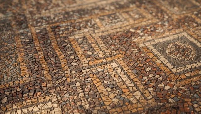 Displaying ancient stone mosaic floor with geometric bands, worn tesserae and medallion