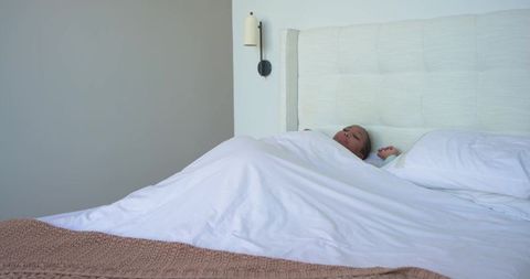 Mid-adult african american woman lying under white duvet on bed in minimalist calm bedroom