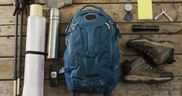Camping equipment with rucksack, boots and thermos on wooden background. National camping month and active lifestyle concept.