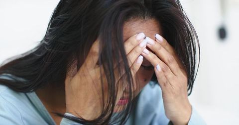 Middle-aged asian woman holding head with hands leaning forward showing stress and fatigue