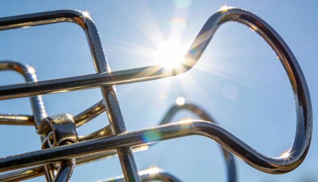 Glinting chrome wireframe catching sun flare over clear blue sky, reflective metal loops